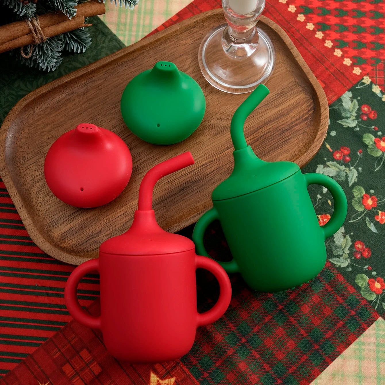 Red and green silicone straw cups with sippy lids on a Christmas table runner