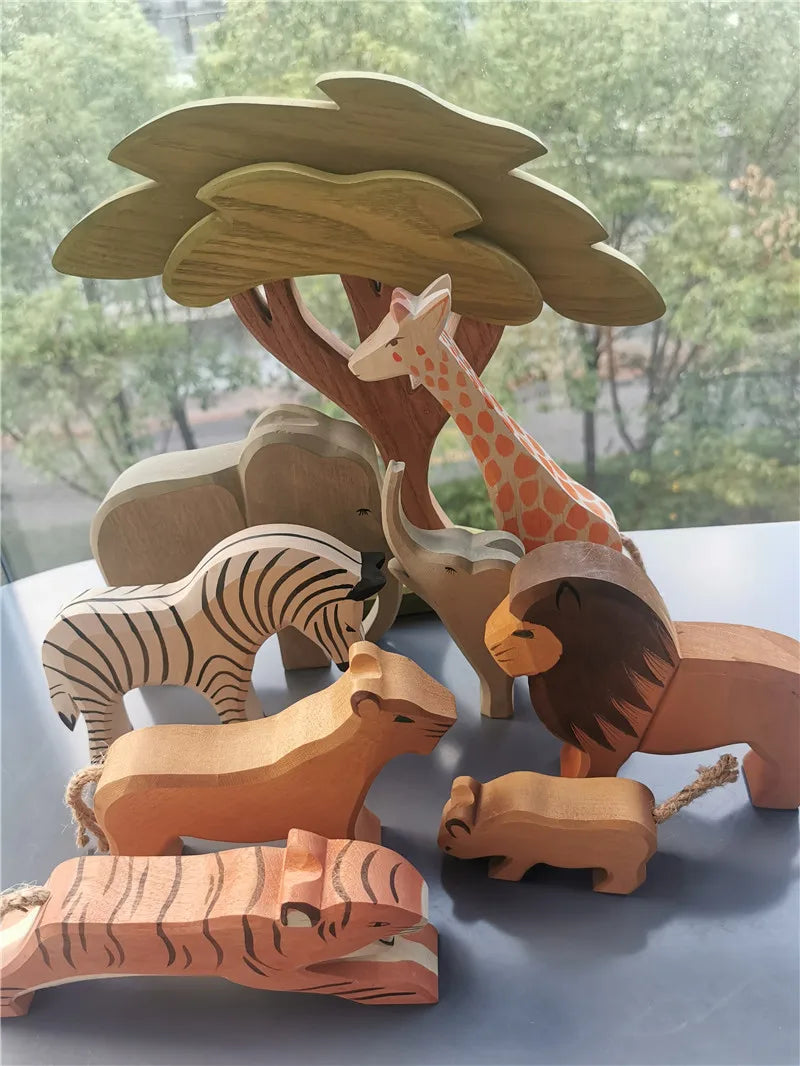 Wooden toy animals including a giraffe, lion, zebra, and tiger under a tree with a blurred outdoor background.