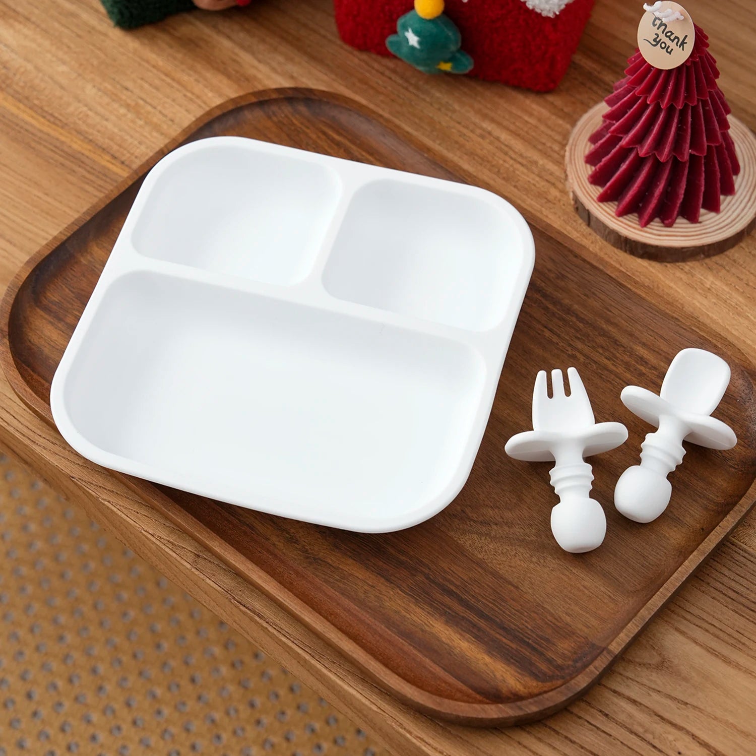 White square silicone suction plate with white spoon and fork on a wooden tray