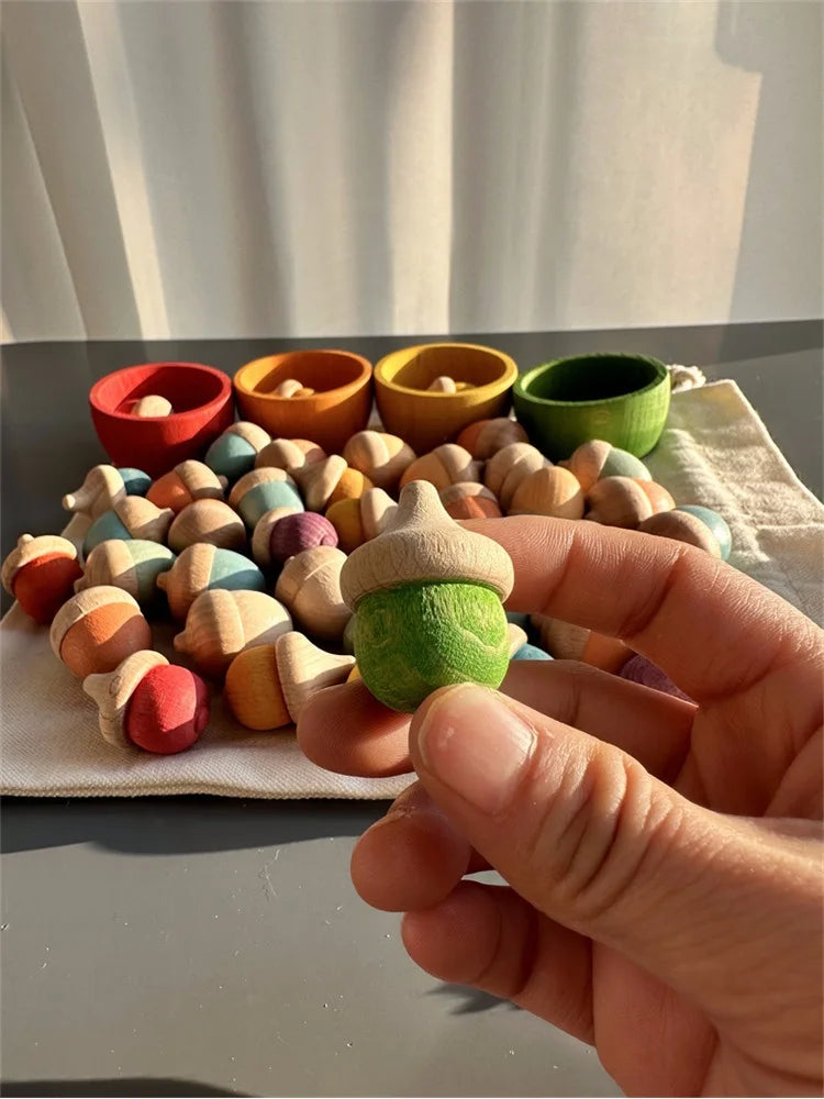 Colorful wooden acorn-shaped toys on a table with a hand holding a green one.