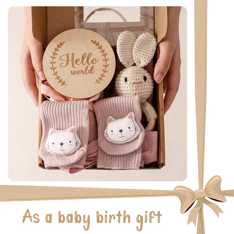 Baby gift set with socks, plush toy, and wooden disc held by hands.