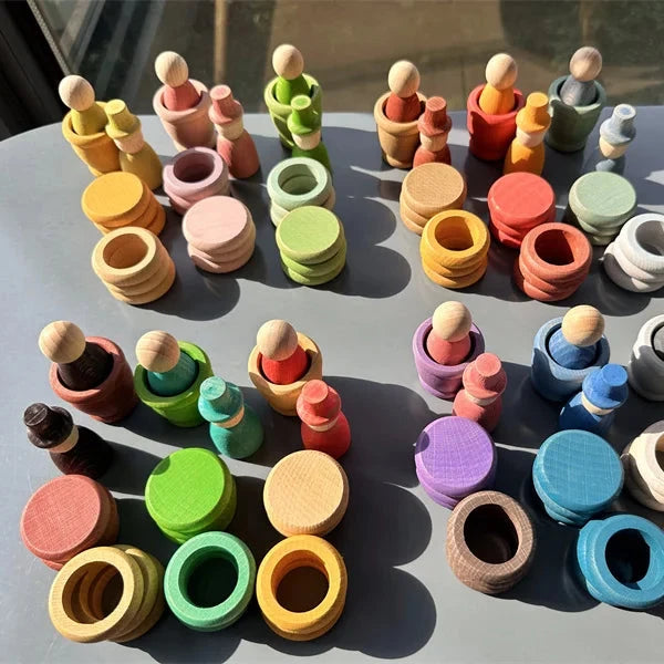 A collection of colorful wooden toy figures and rings arranged on a gray table in bright natural sunlight.