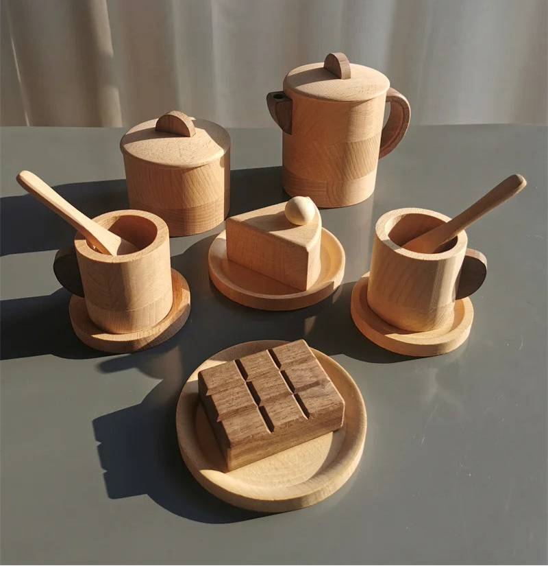 Set of wooden kitchen utensils including pots, spoons, and a knife on a gray surface with a white curtain background.