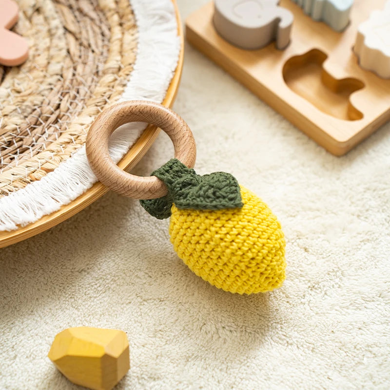 Yellow knitted toy with a wooden ring on a textured surface