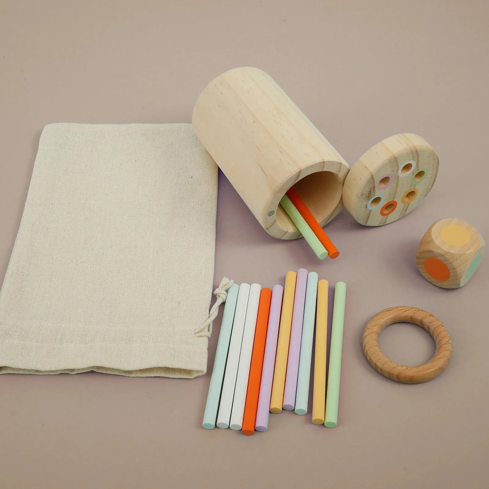 Set of wooden toys including a cylindrical container with colorful sticks and a ring on a beige background