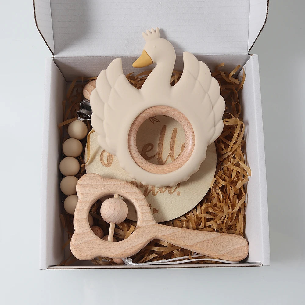 Set of wooden baby toys including a swan rattle and a wooden ring with 'hello' engraving, presented in a box.