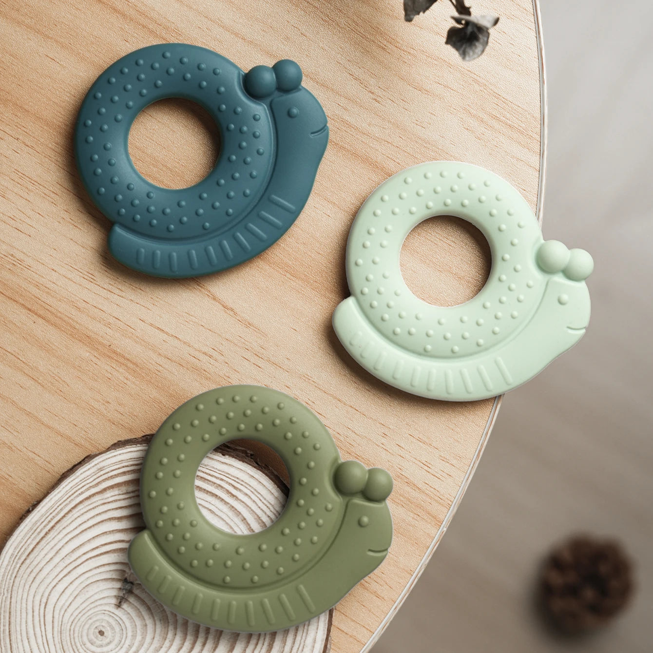 Teal, mint and olive snail silicone teethers on a wooden table
