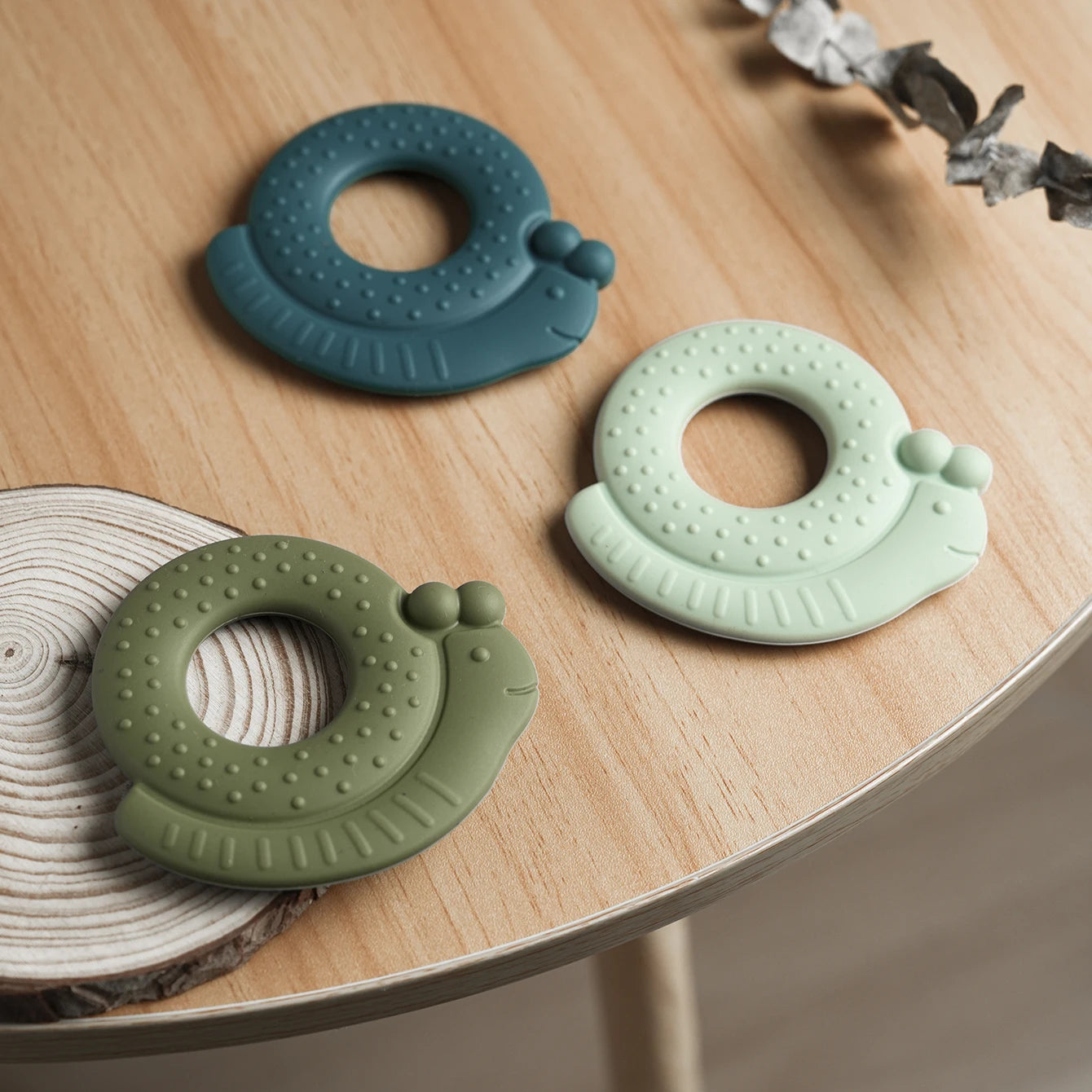 Three snail silicone teethers on a wood slice
