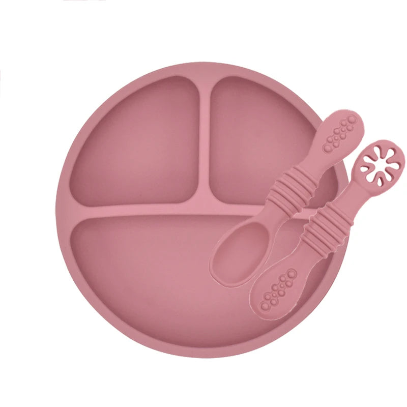 Pink silicone plate with divided sections and a spoon on a white background