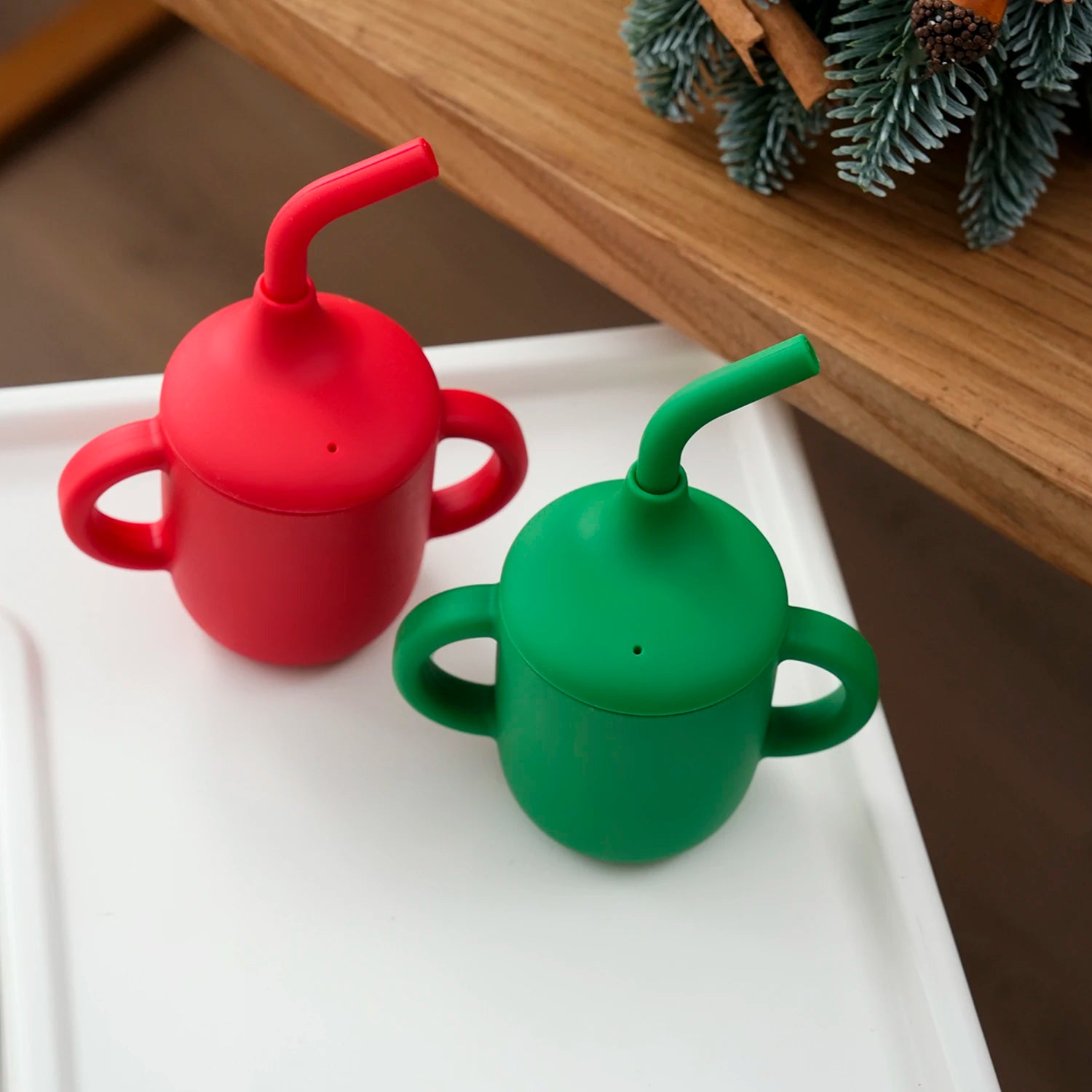Red and green silicone straw cups with double handles on a white high chair tray