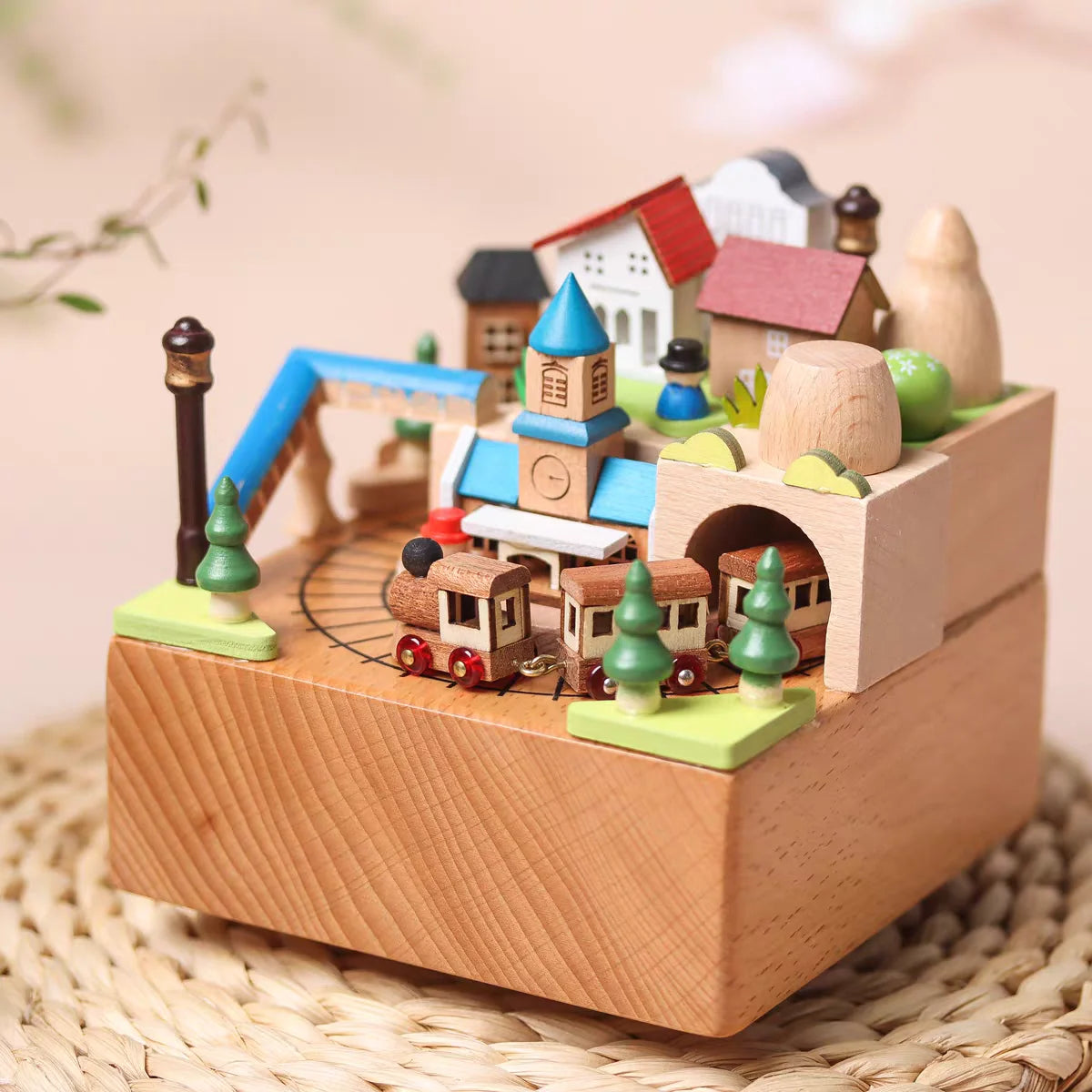 Wooden toy village with houses, a clock tower, and a train on a woven surface.