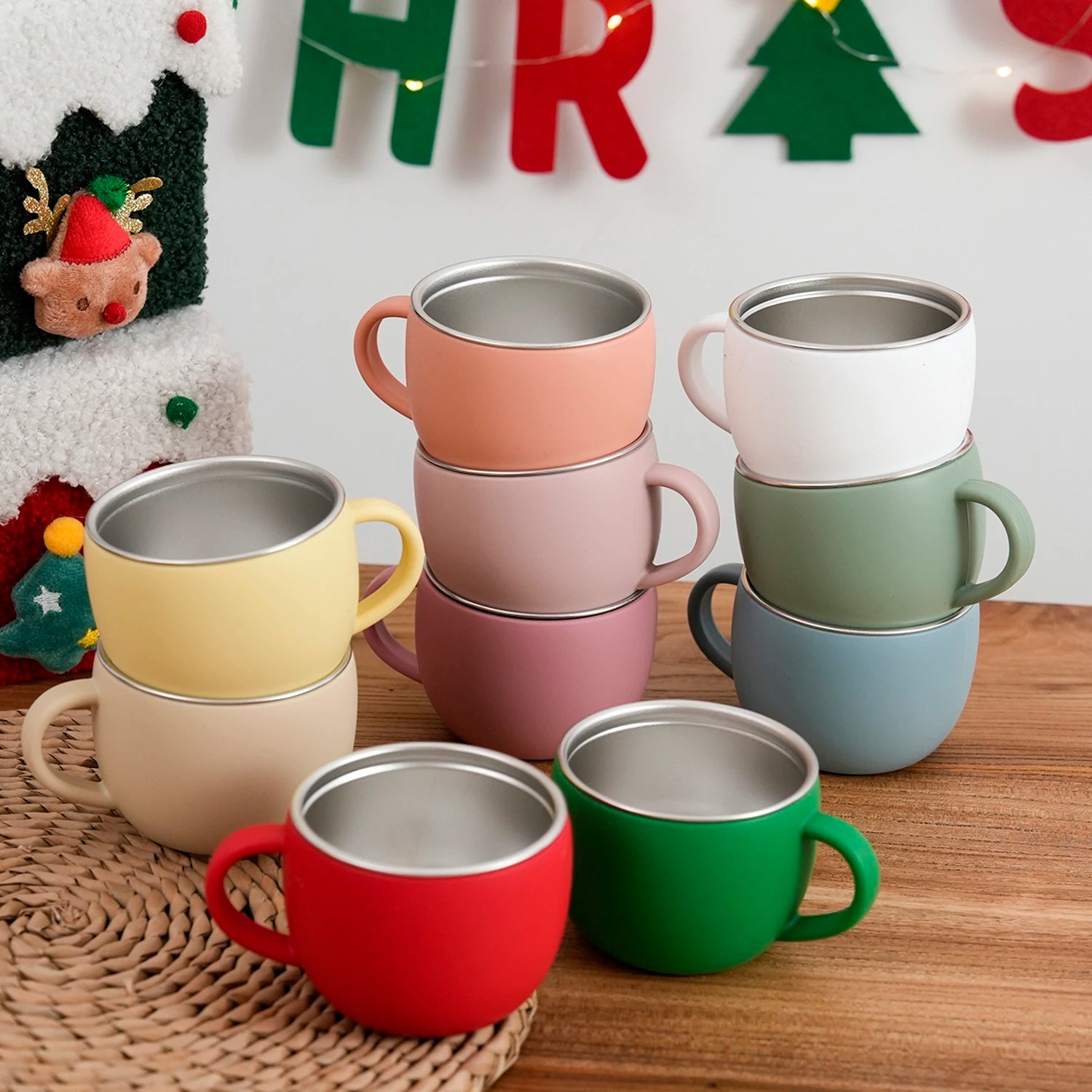 Stainless steel and silicone toddler mugs stacked in front of a Christmas banner