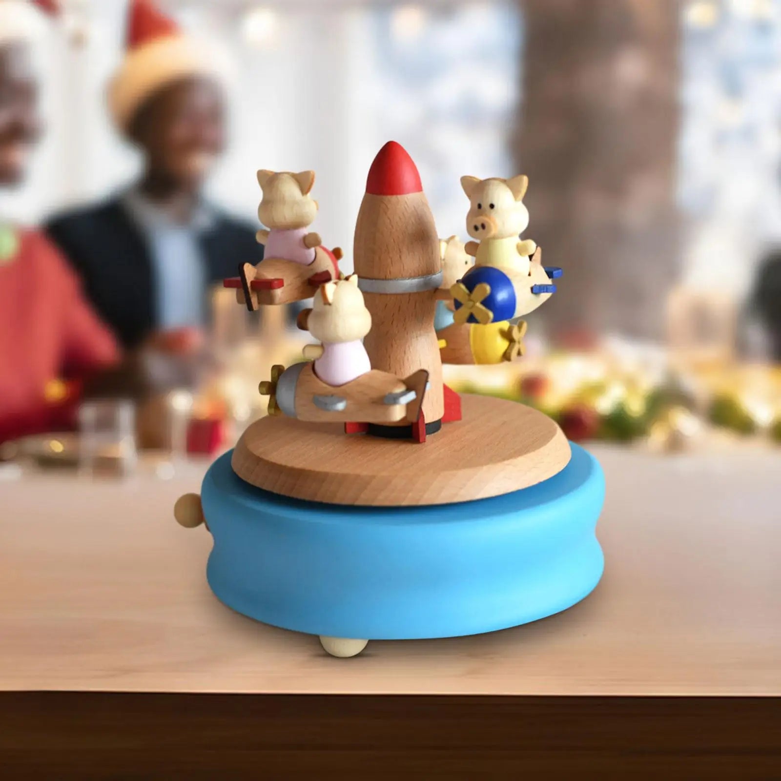Wooden toy with a rocket and animal figures on a blue base, blurred people in the background | Oliver & Company Montessori Toys
