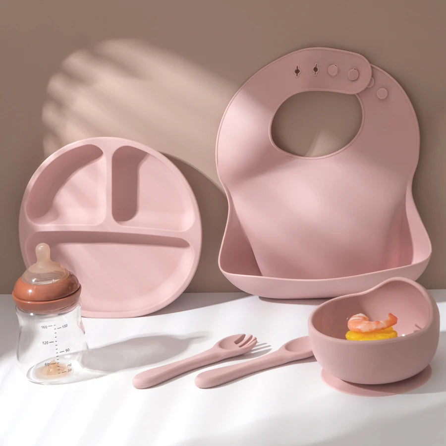 Light pink bib, divided plate, bowl, spoon and fork on a table