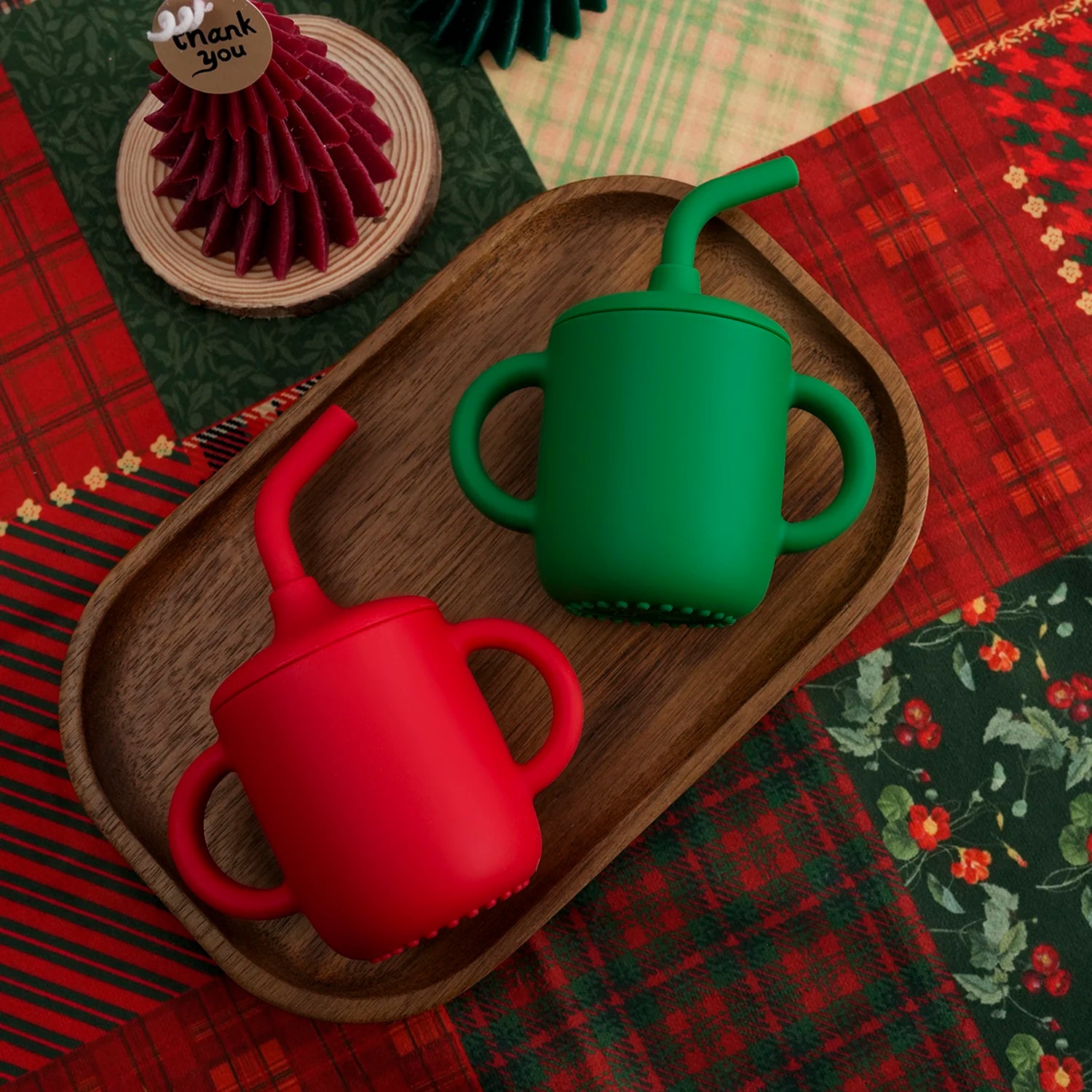 Red and green silicone straw cups on a wooden tray with Christmas plaid
