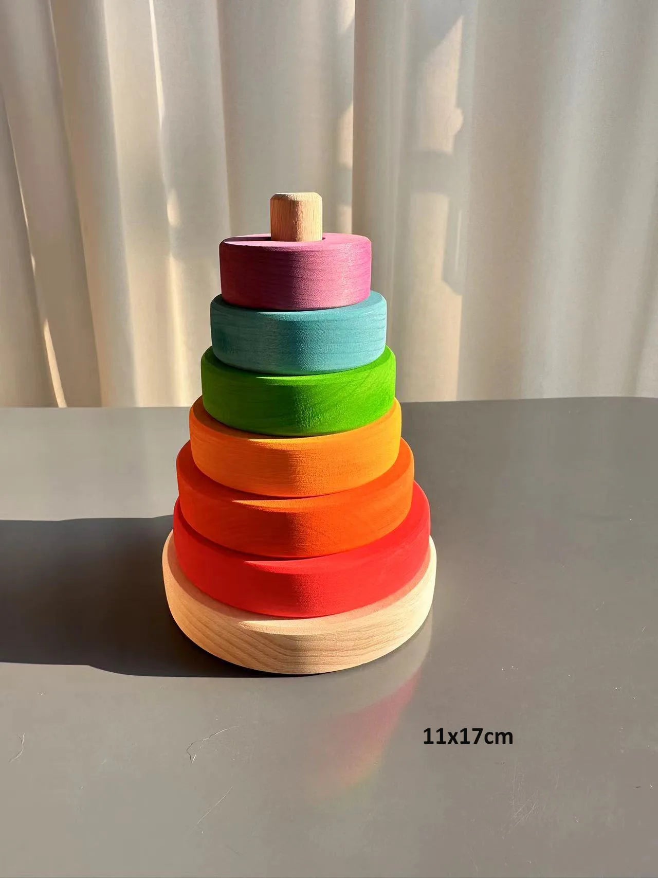 Colorful wooden stacking toy on a gray surface with a white curtain background