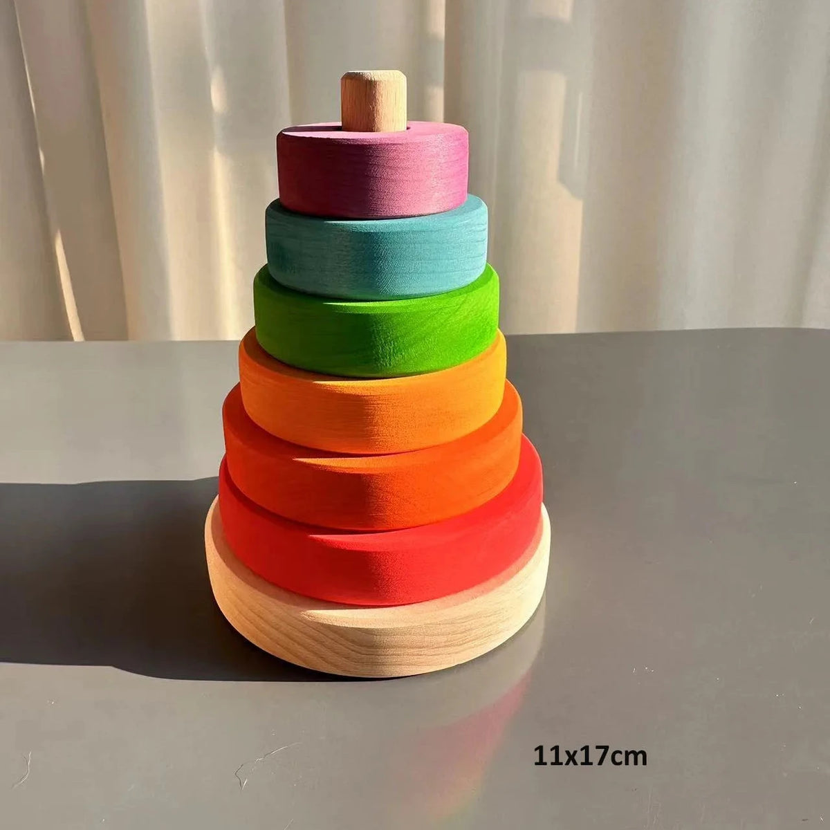 Colorful wooden stacking toy on a gray surface with a white curtain background