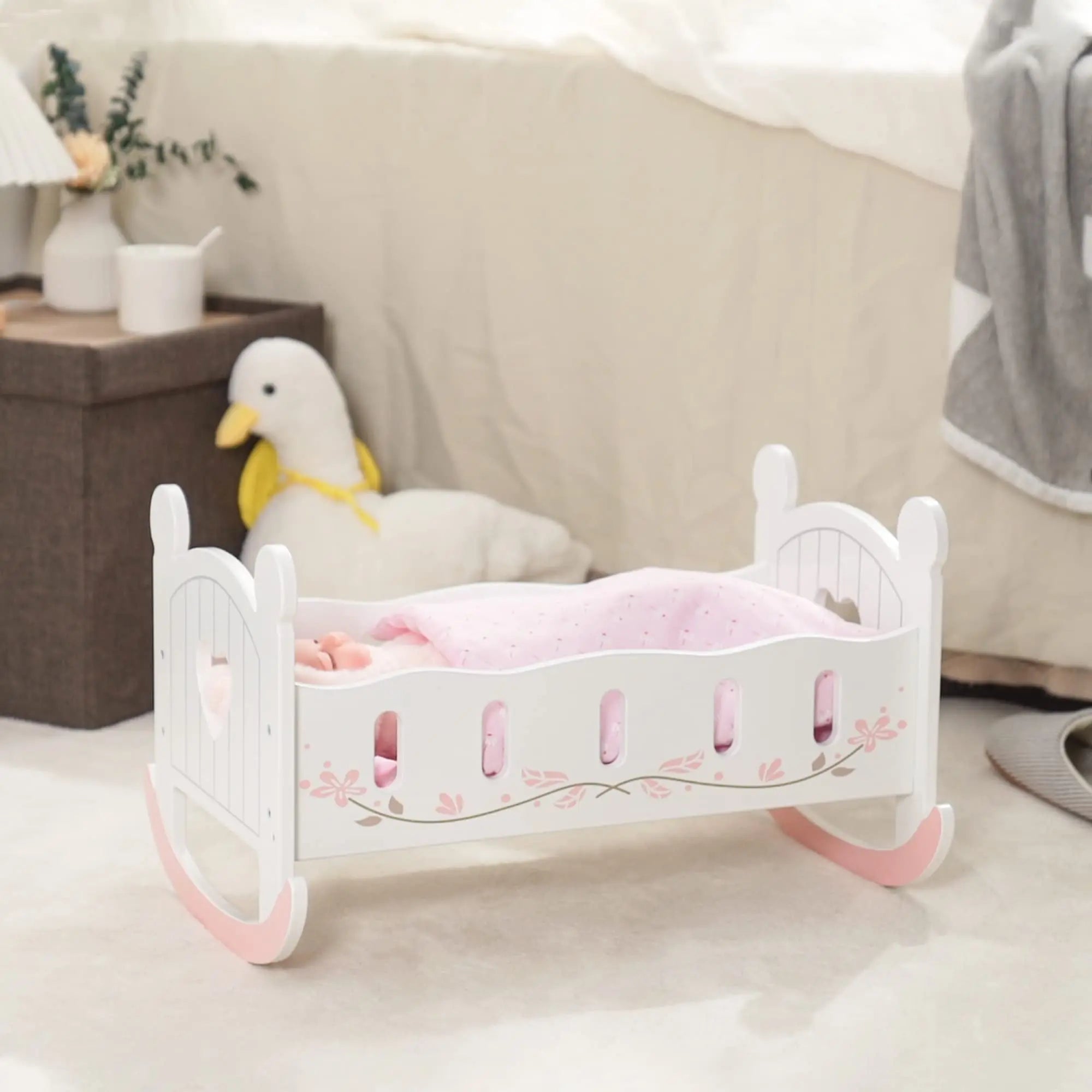 Small white and pink rocking crib with pink bedding on a light-colored floor.