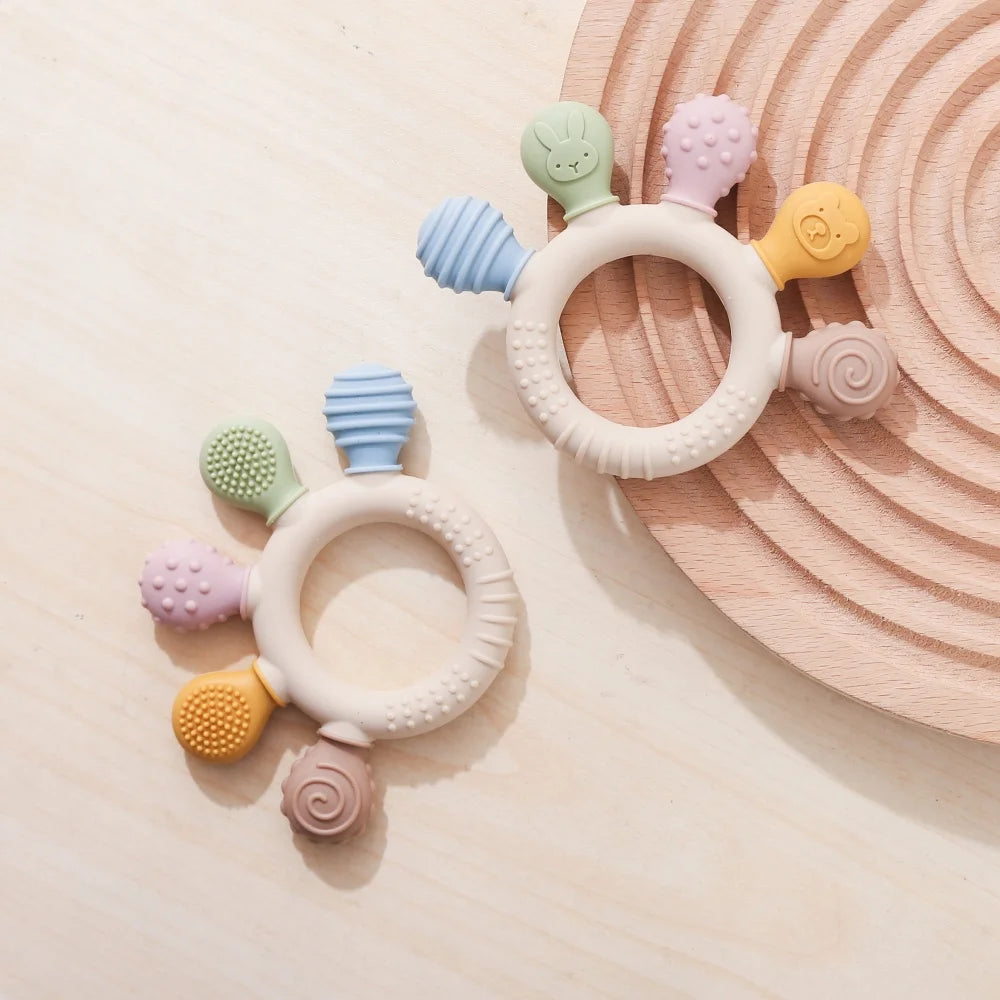 Two colorful baby teething rings on a light beige surface with a wooden disc in the background.
