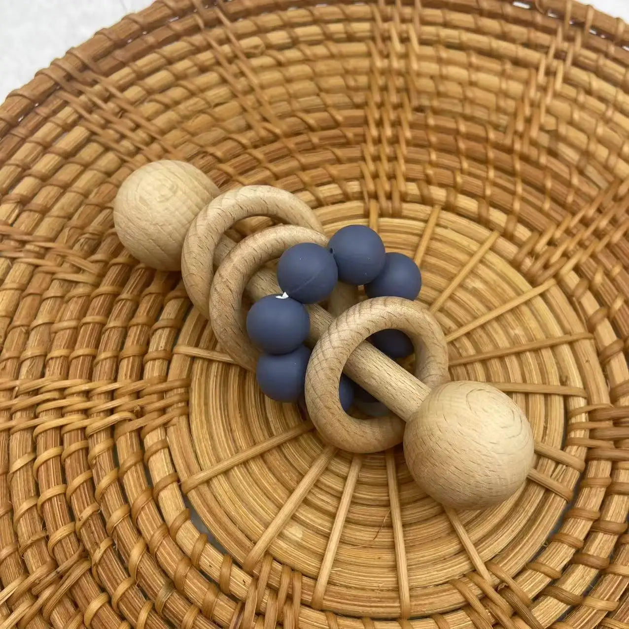 Wooden and silicone baby rattle on a woven surface