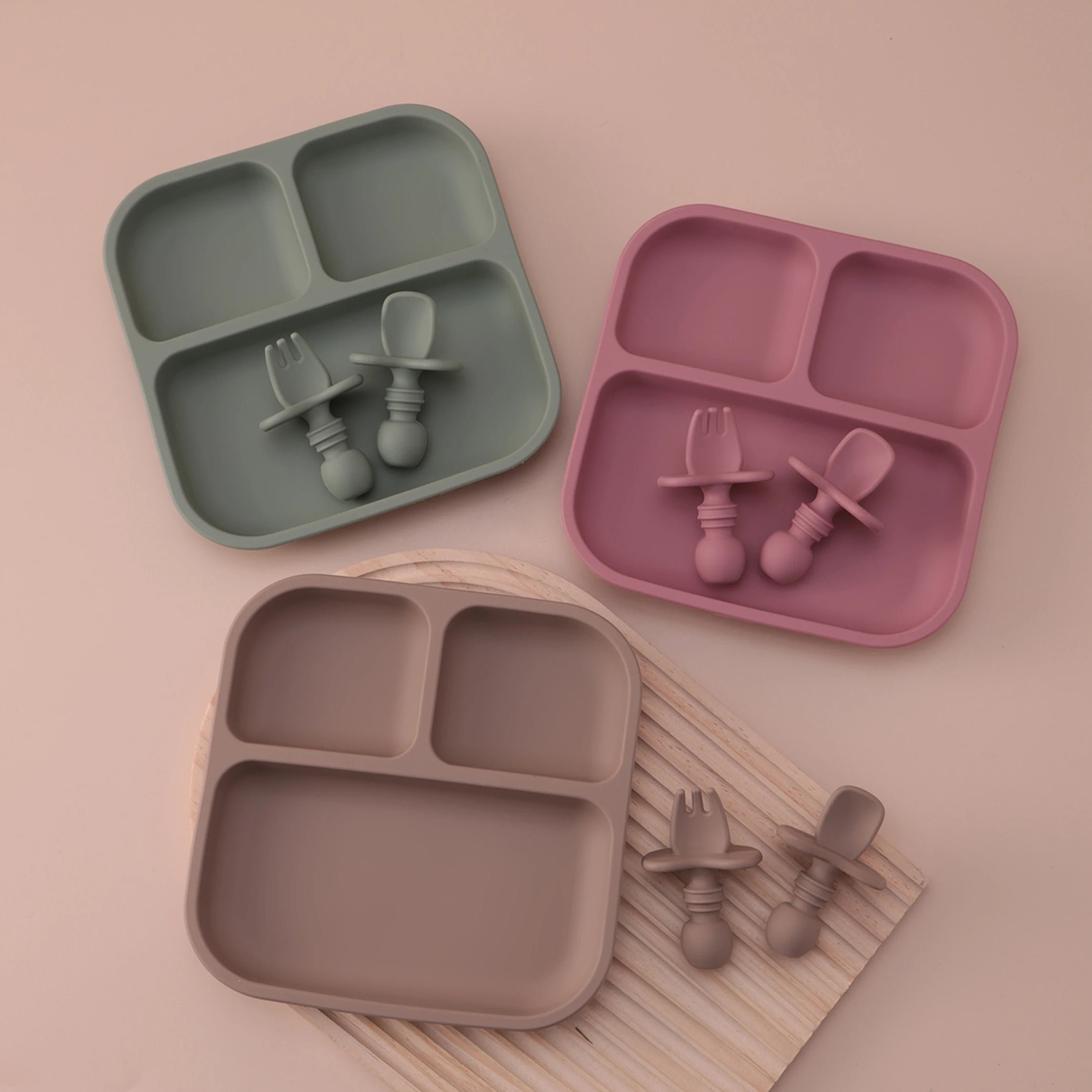 Three silicone吃饭 sets in green, pink, and brown on a beige background