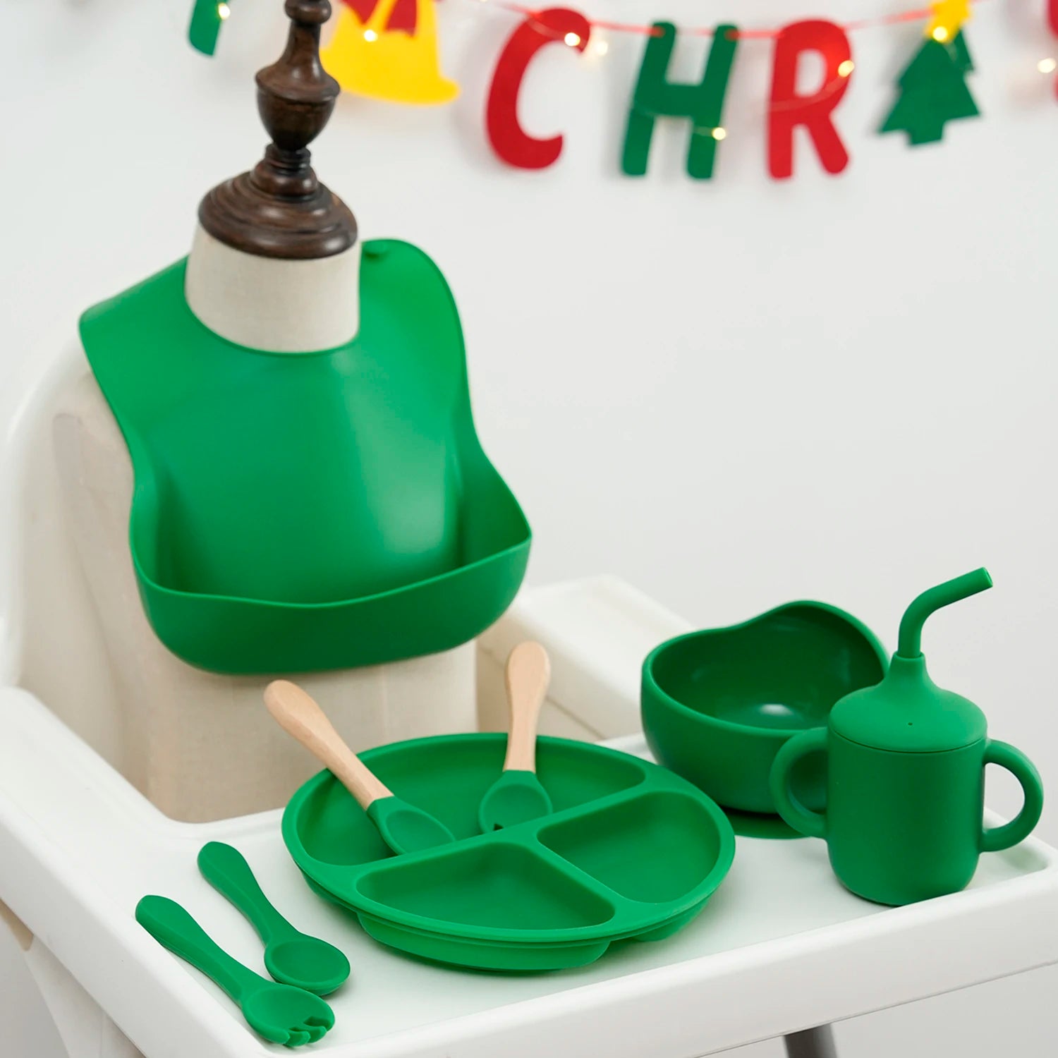 Green 8-piece silicone feeding set on a high chair in front of a Christmas banner