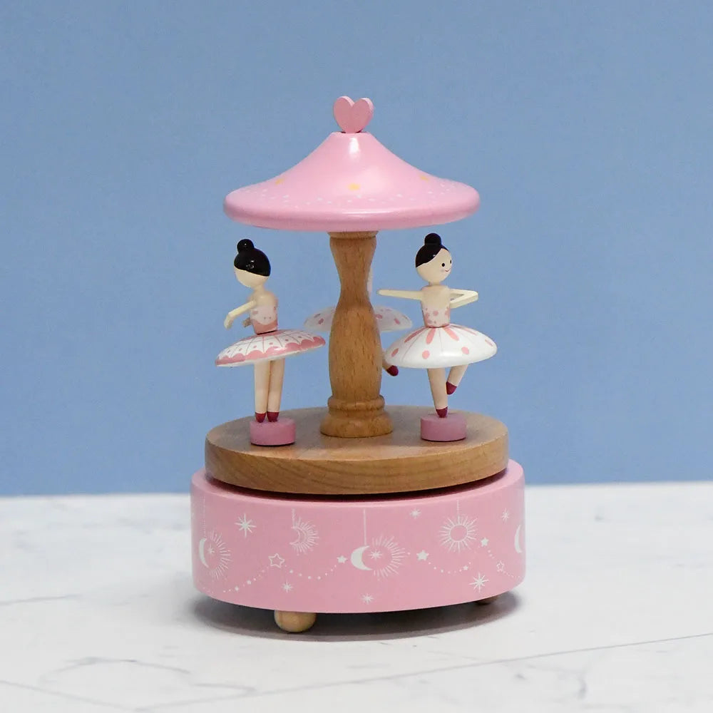 Wooden carousel toy with ballerina figures on a pink base against a blue background