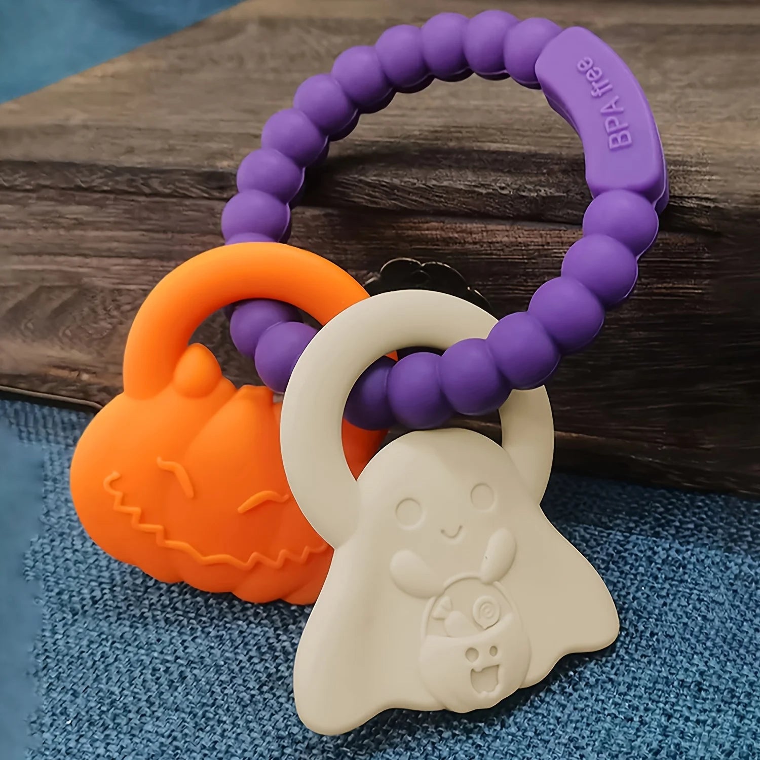 Purple, orange, and white teething toys on a wooden surface with blue fabric underneath.