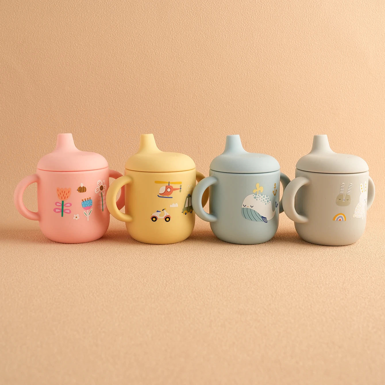 Four cartoon silicone sippy cups in pink, yellow, blue and cream