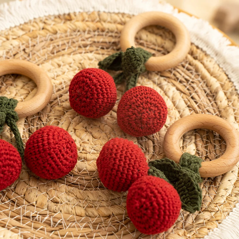 Crocheted red berries with wooden rings on a woven surface