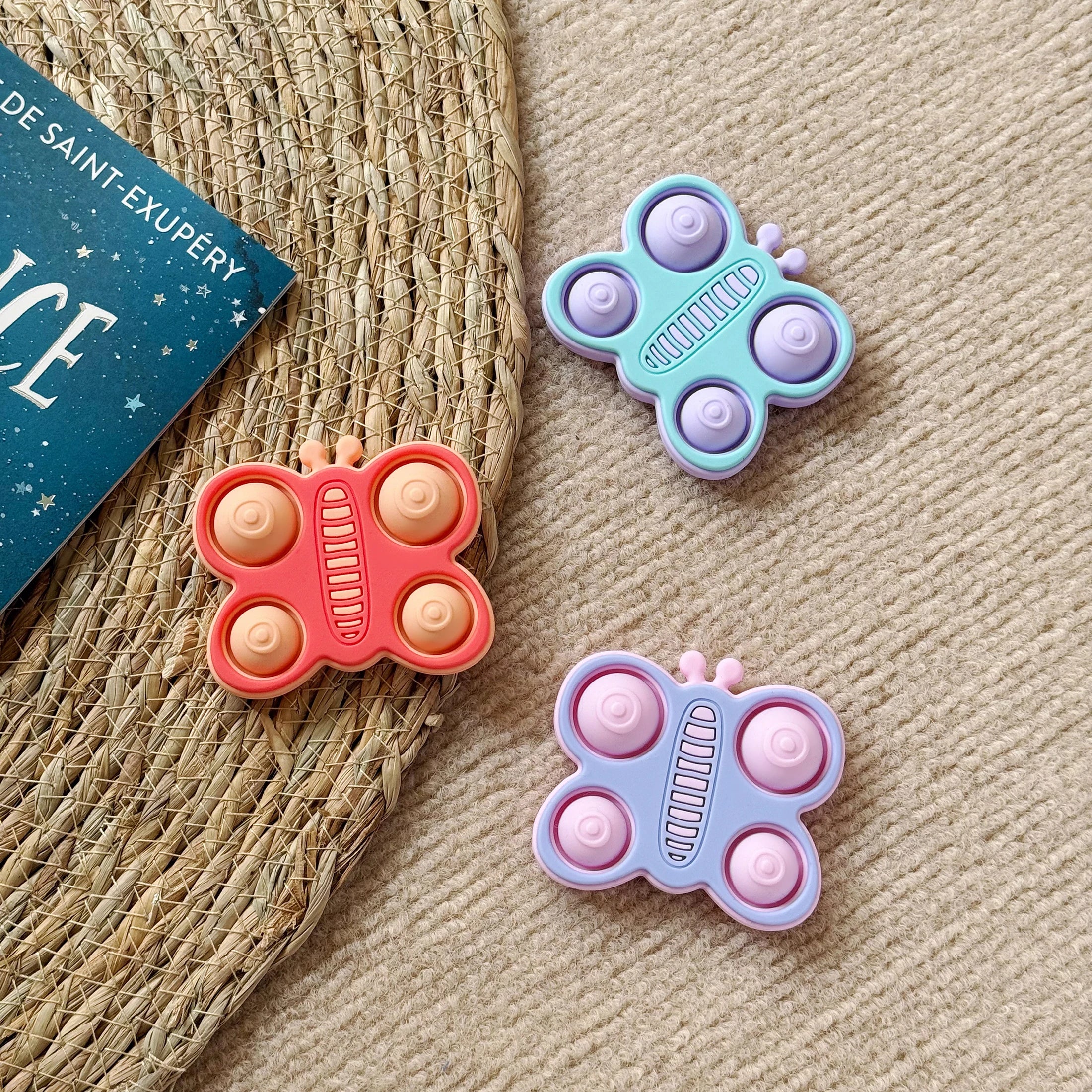 Three butterfly silicone teethers on a woven mat