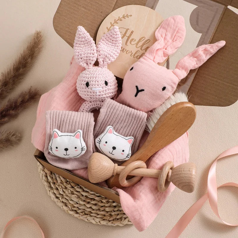 Baby gift set with pink bunny toys, socks, and a wooden rattle in a basket.