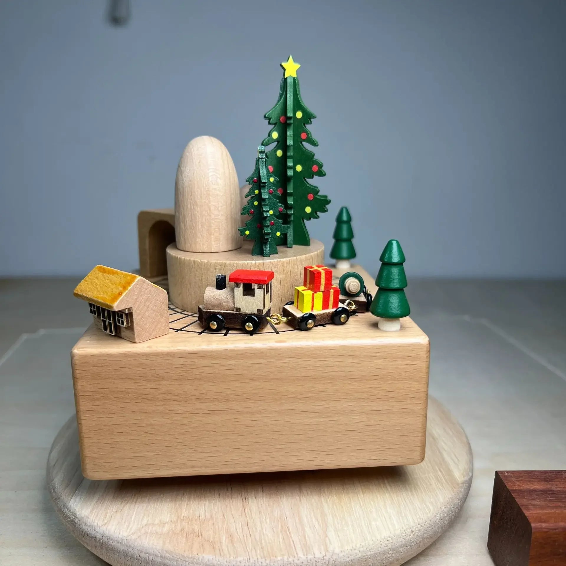 Wooden toy set with a Christmas tree, houses, and a train on a gray surface.