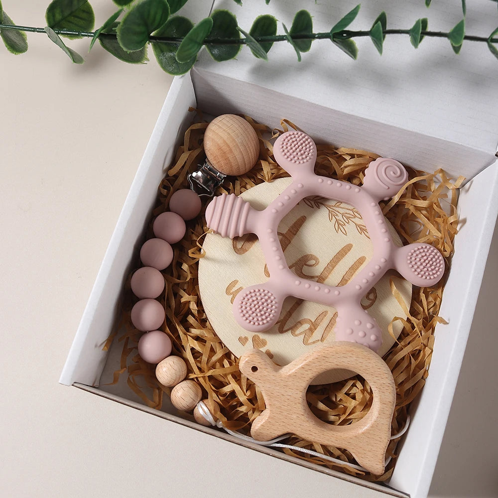 Pink and wooden baby teething toys in a gift box with decorative elements.