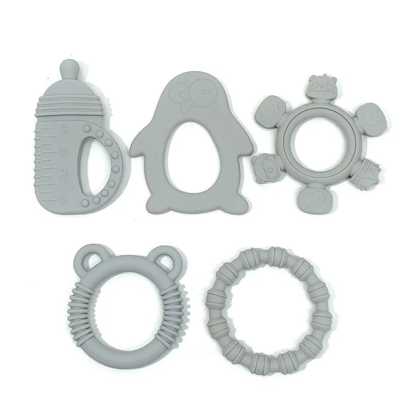 Six gray silicone baby teething toys arranged on a plain white background, including a bottle-shaped ring, a penguin-shaped ring, a flower-shaped ring with animal faces, and two textured circular tees.