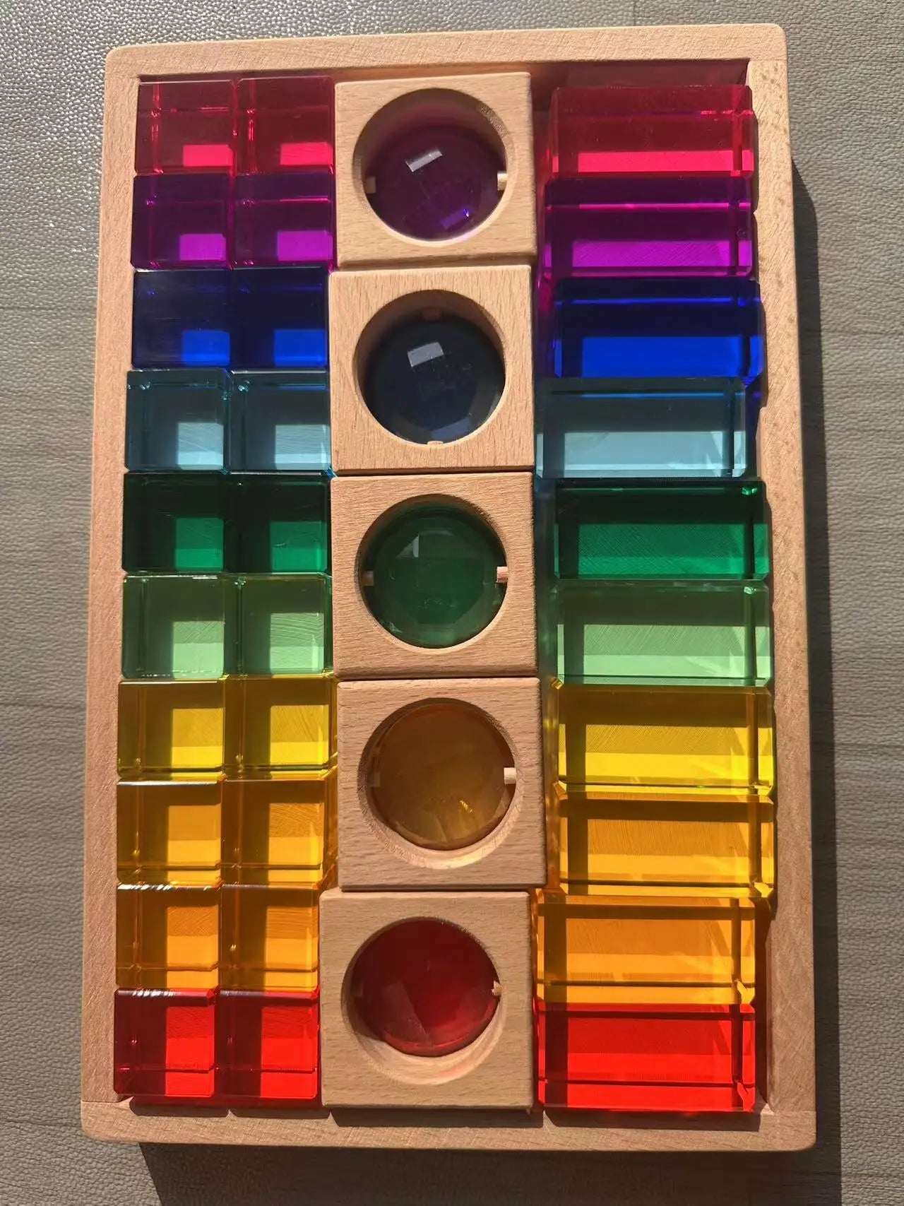 Colorful transparent blocks in a wooden puzzle box on a wooden surface