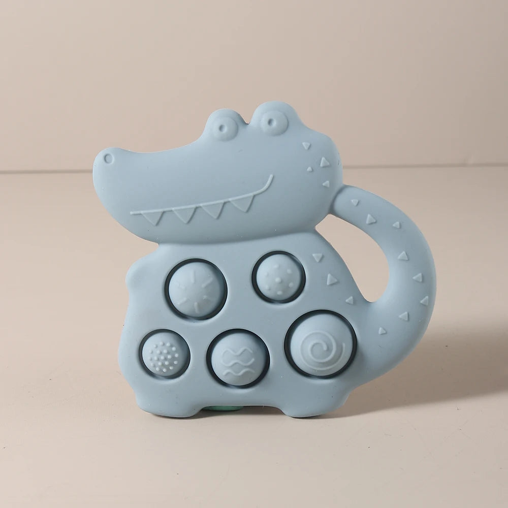 Light blue crocodile-shaped teething toy with textured buttons on a beige background