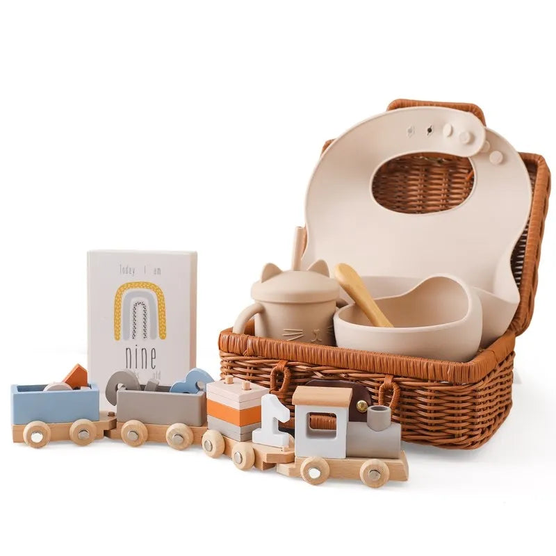 Baby Birthday Train Toy & Silicone Bib Gift Set featuring a wooden train, silicone bib, learning cup, and photography props in a wicker basket.