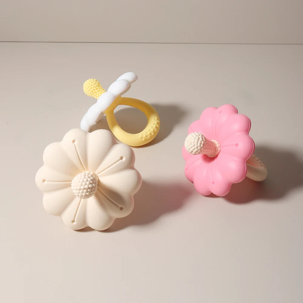Two flower-shaped baby teething toys, one pink and one beige, on a light background.