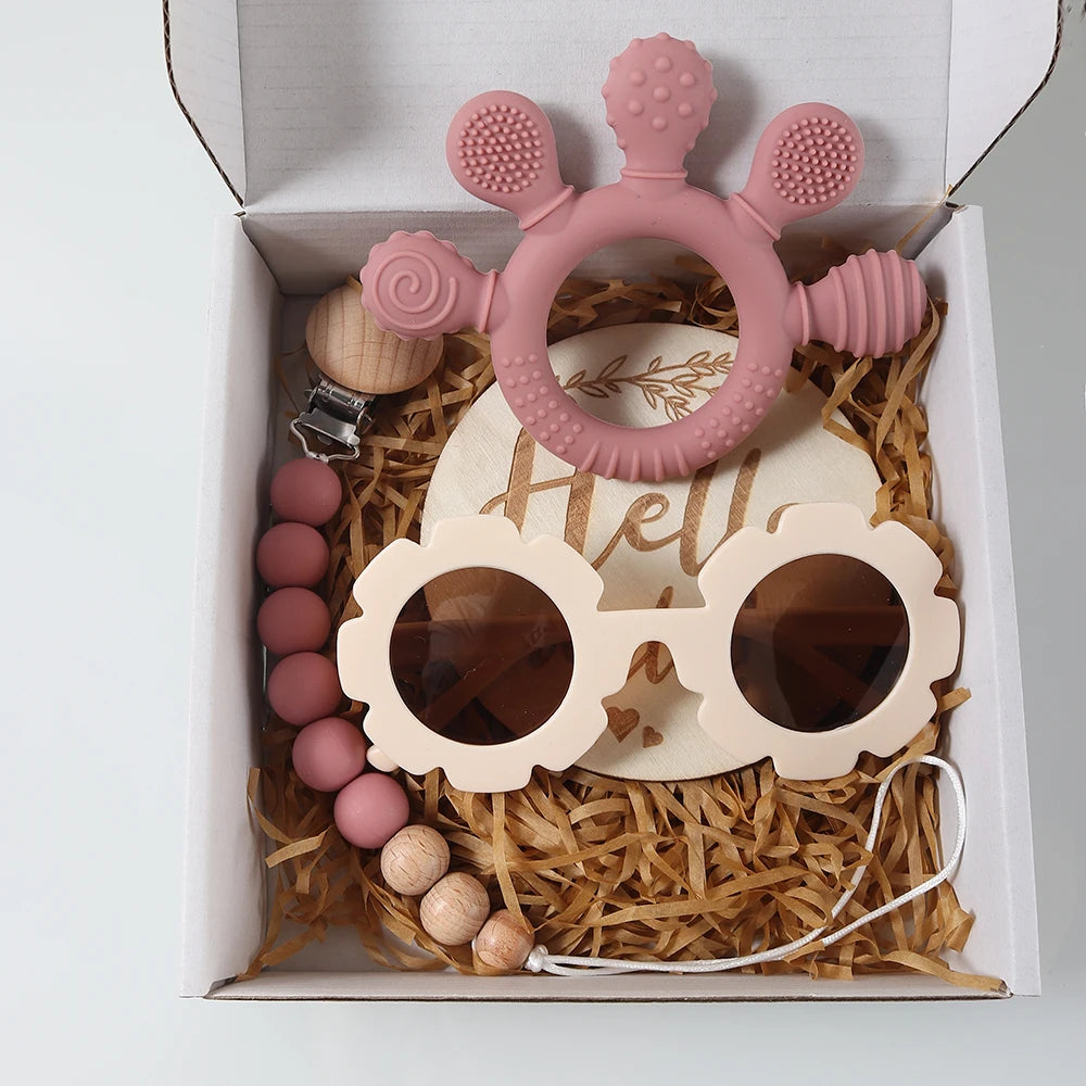 Baby teething toy set with pink ring, wooden sunglasses, and beads in a gift box.