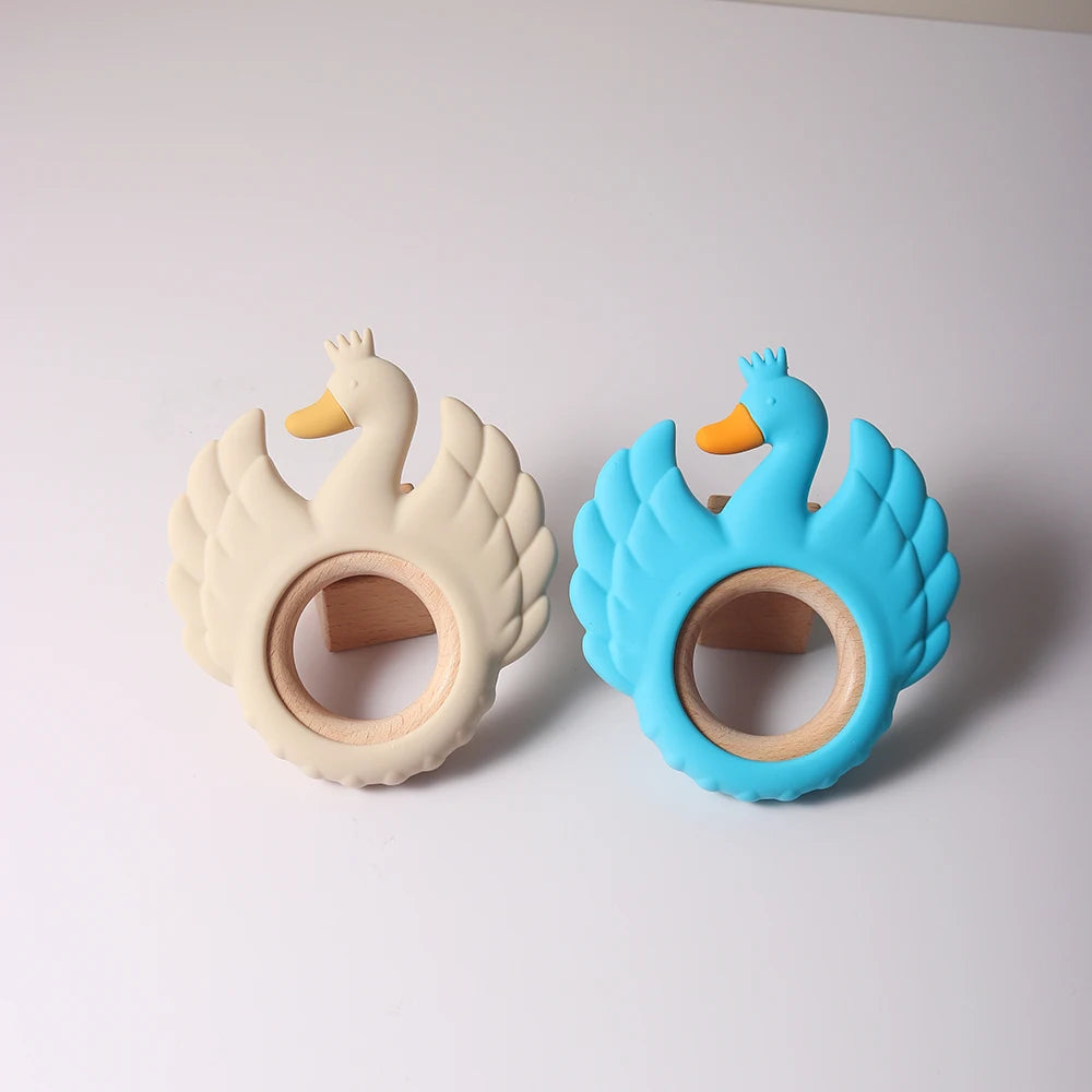 Two swan-shaped baby teething rings, one beige and one blue, on a light gray background.