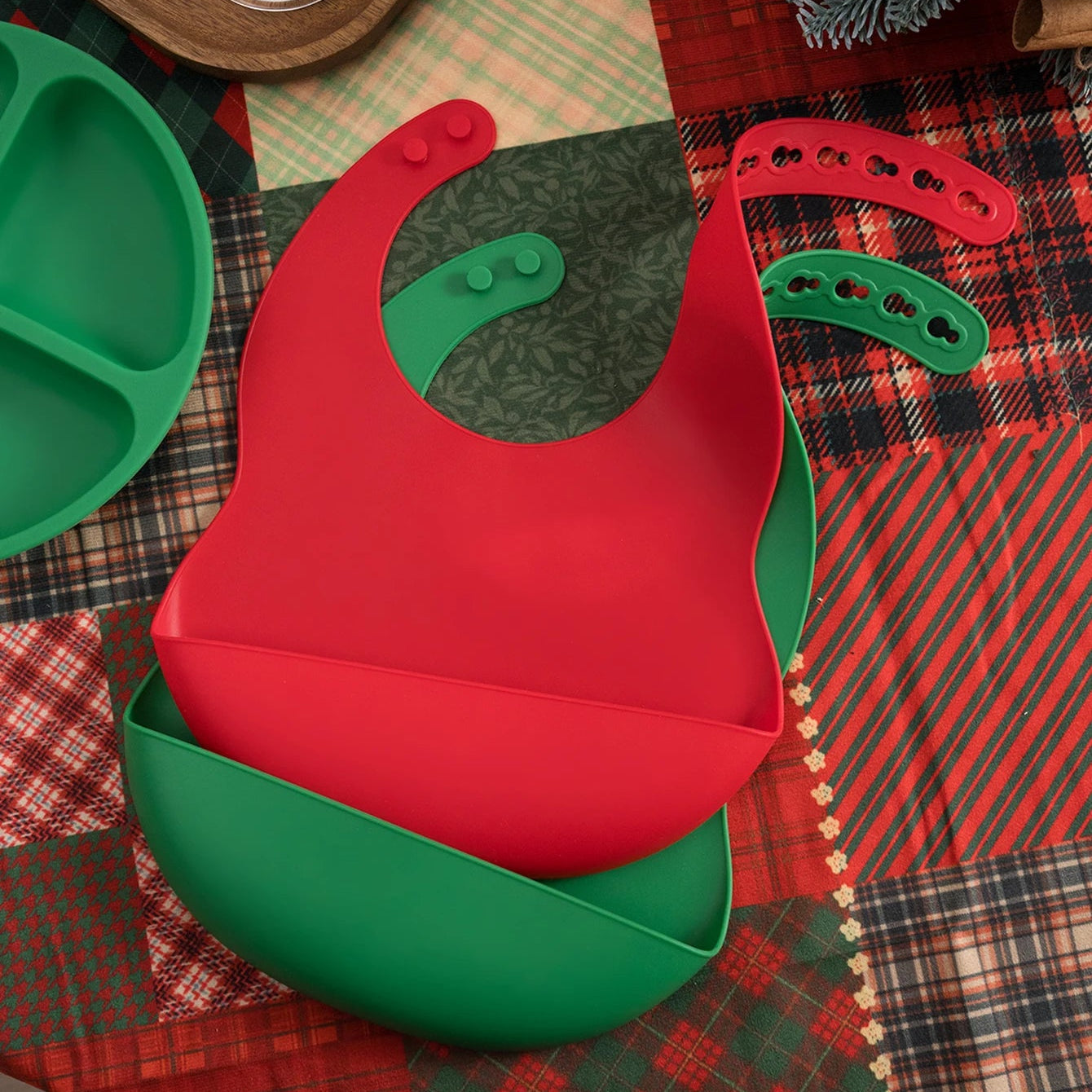 Red and green silicone baby bibs on a Christmas plaid tablecloth