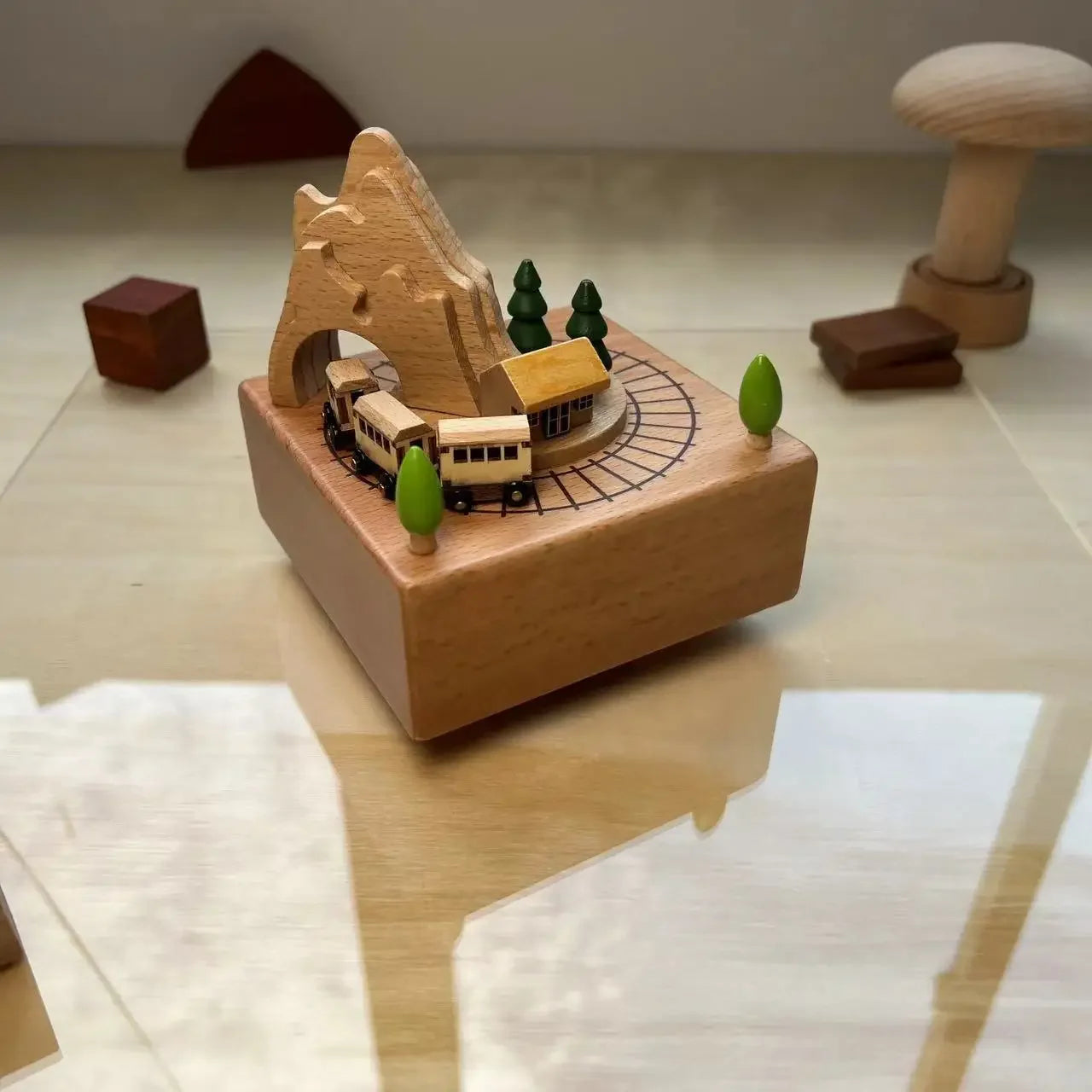 Wooden toy train set with mountains and trees on a reflective surface