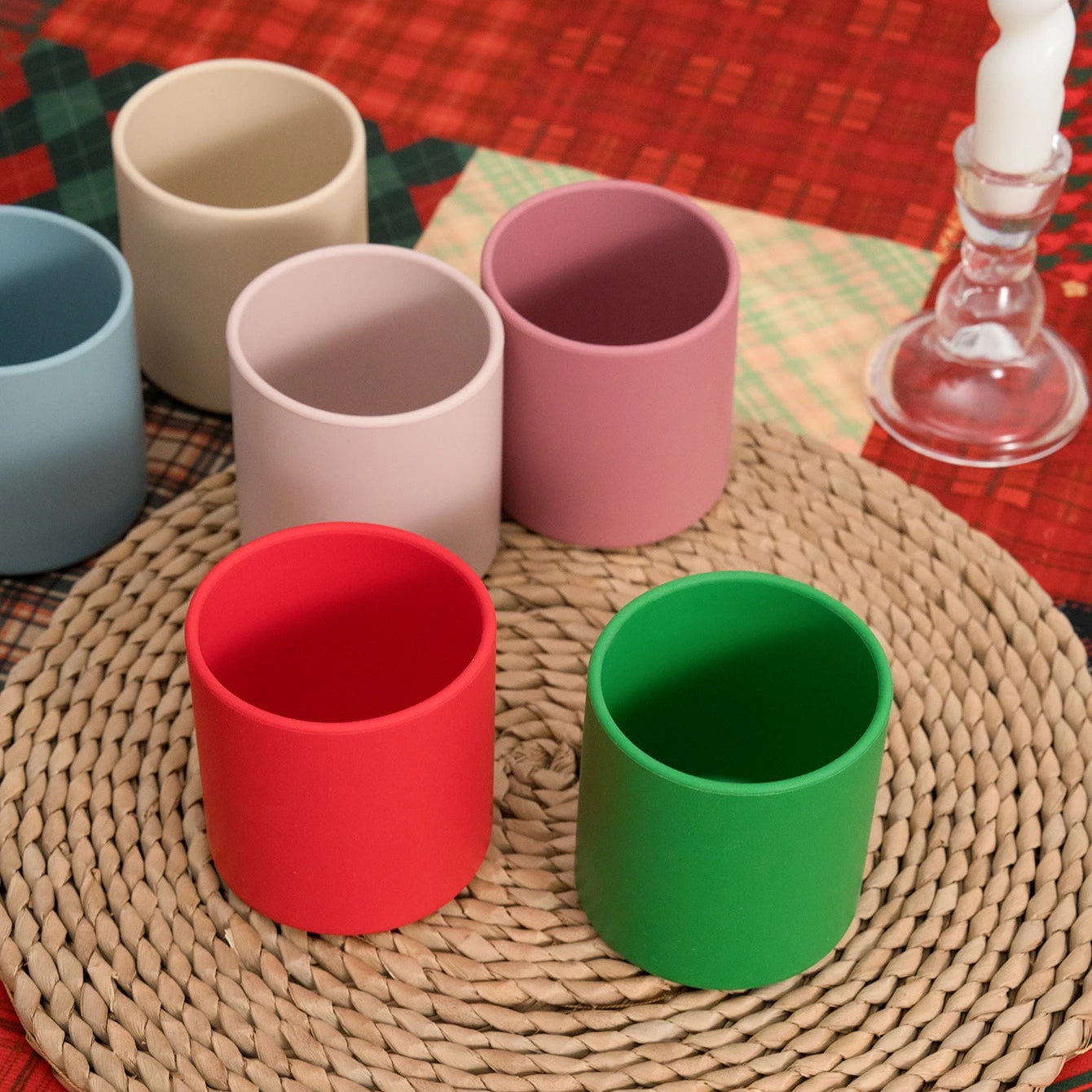 Red and green silicone open cups on a woven placemat with Christmas plaid