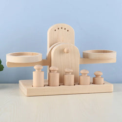 Wooden Balance Scale Toy with weights and a plant on a wooden surface, ideal for educational play and developing children's balance and numerical skills.