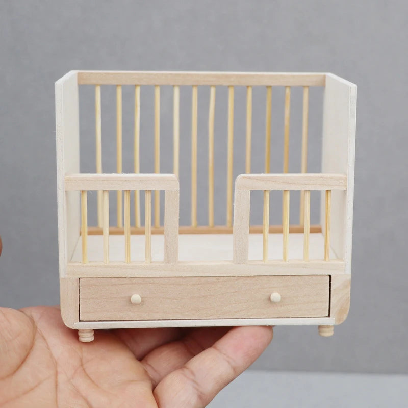 Miniature wooden crib with a drawer held in a hand against a gray background