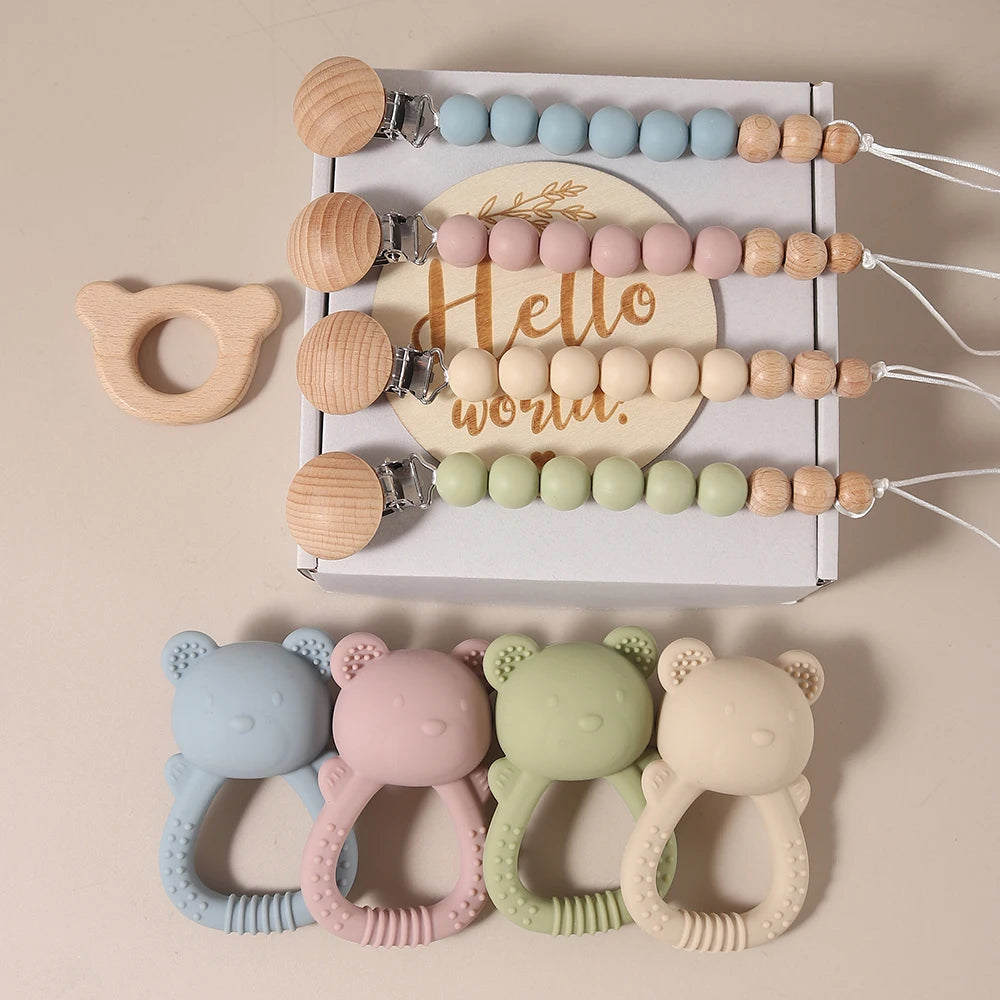 Set of baby teething toys with wooden and silicone designs, including a 'Hello world.' message, on a beige background.
