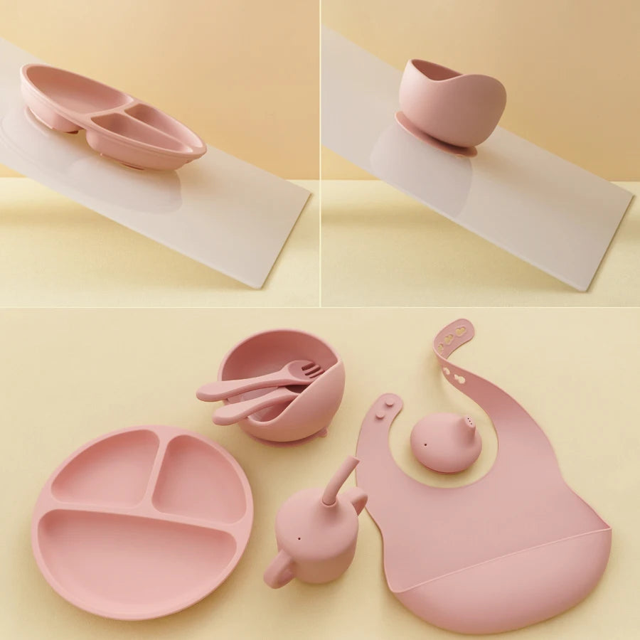 A coordinated baby feeding set in soft dusty pink silicone, shown across a four-panel collage. The set includes a divided plate, suction cup bowl, small bowl with spoon, teapot, bib, and a small cup or teapot accessory, all photographed on a pale cream background.