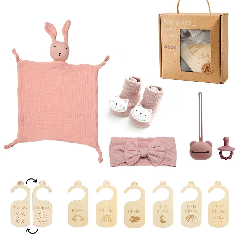 Collection of baby items including a pink comfort blanket, booties, headband, and other accessories on a white background.