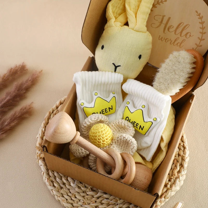 Baby toy and clothing set with a plush bunny, wooden rattle, and socks in a woven basket.